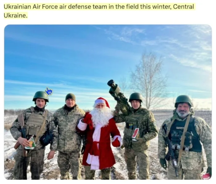 Five Ukrainian soldiers in winter camouflage gear and helmets stand outdoors in a snowy field under a clear blue sky. One…