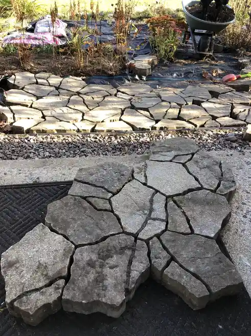 An outdoor photo shows a newly installed concrete driveway with large, irregularly shaped slabs that are visibly cracked and…