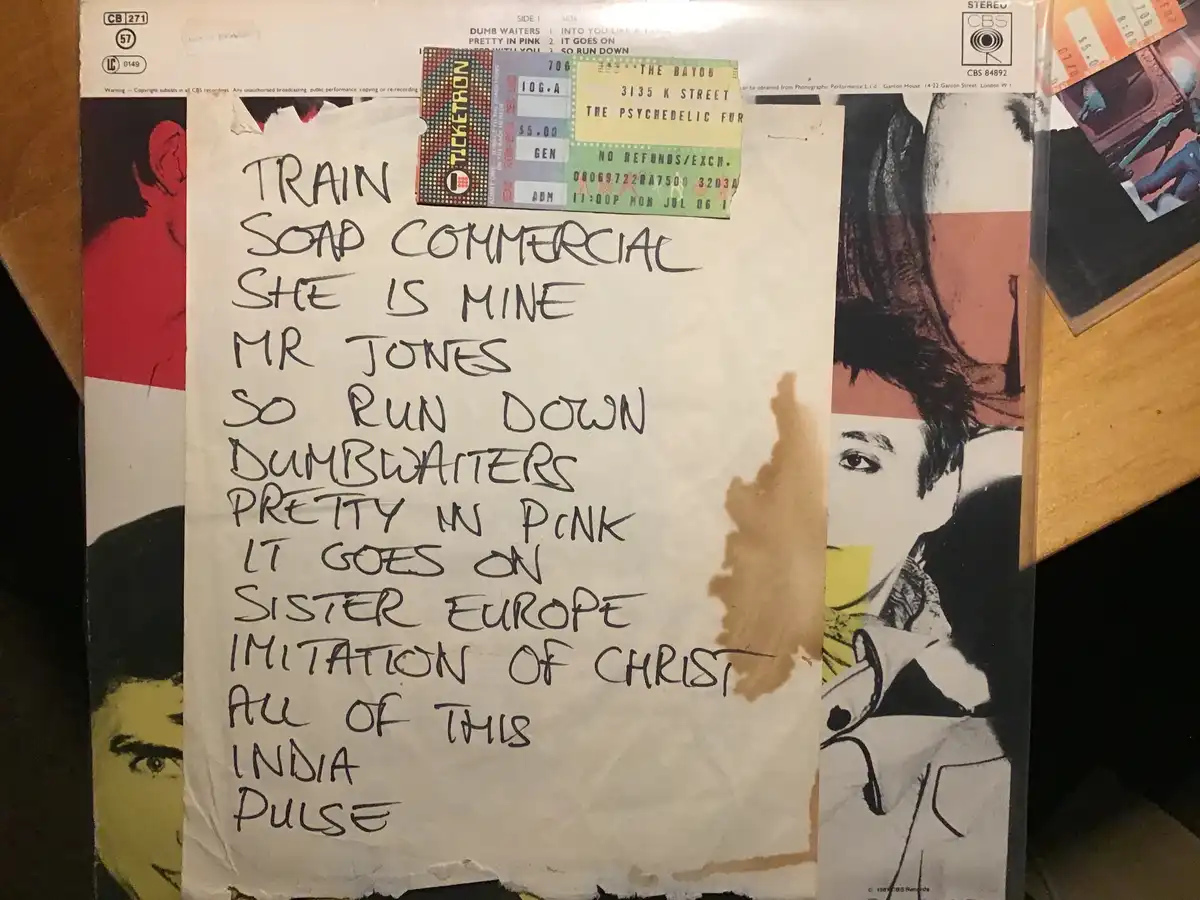 A handwritten list of song titles like 'Train', 'She Is Mine', and 'Pretty in Pink' is taped over a vintage album cover. A…