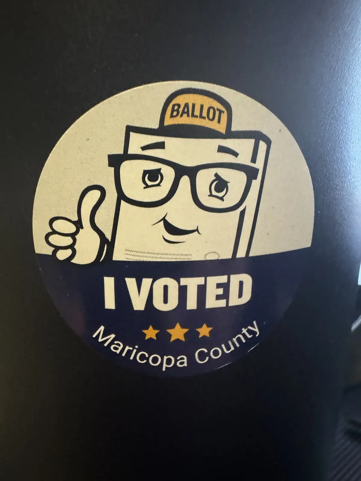A circular 'I VOTED' sticker from Maricopa County features a cartoon ballot box with glasses and a 'BALLOT' hat giving a…