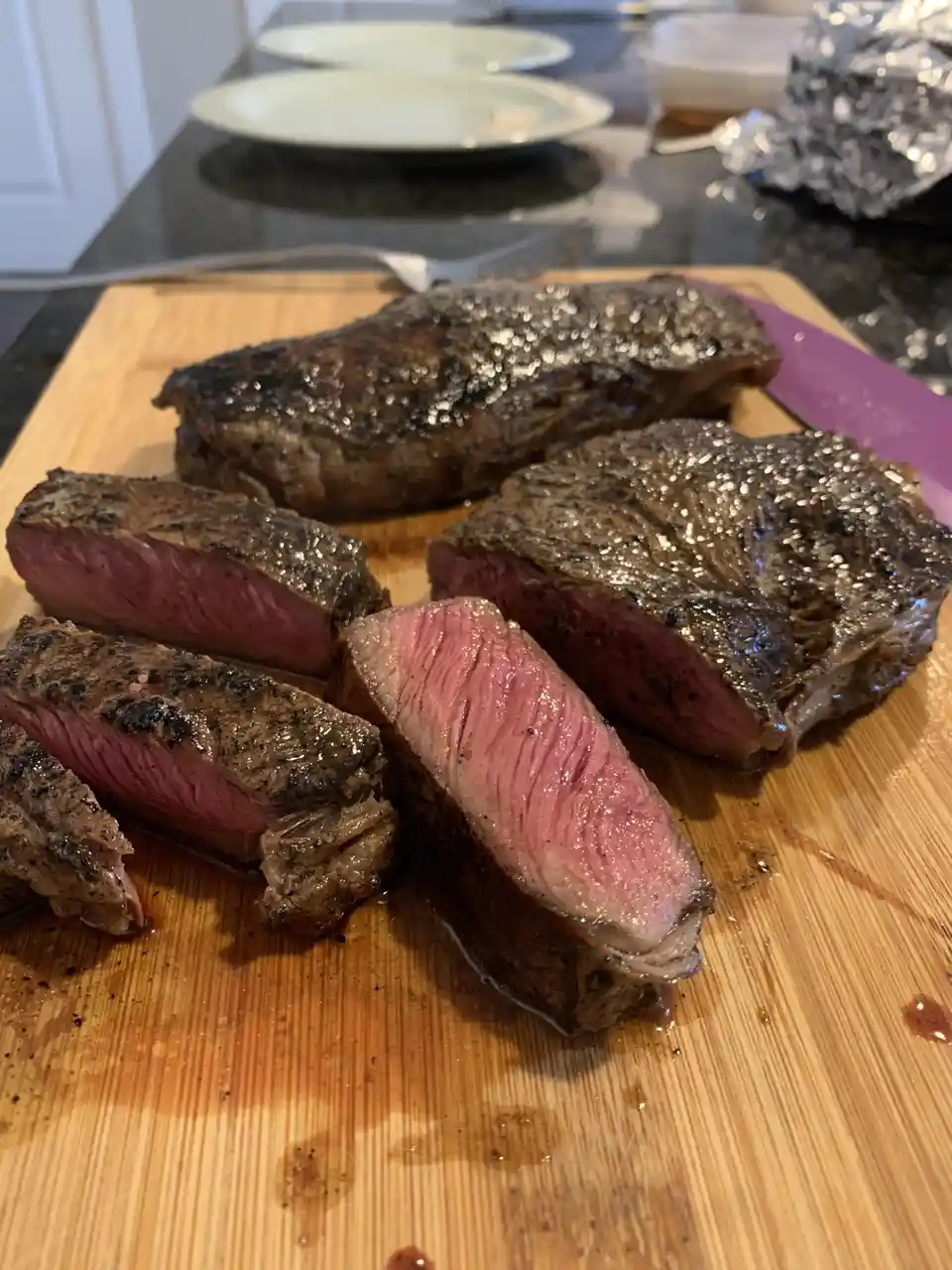 A close-up photo shows a grilled steak sliced into thick pieces on a wooden cutting board, revealing a juicy pink center and…
