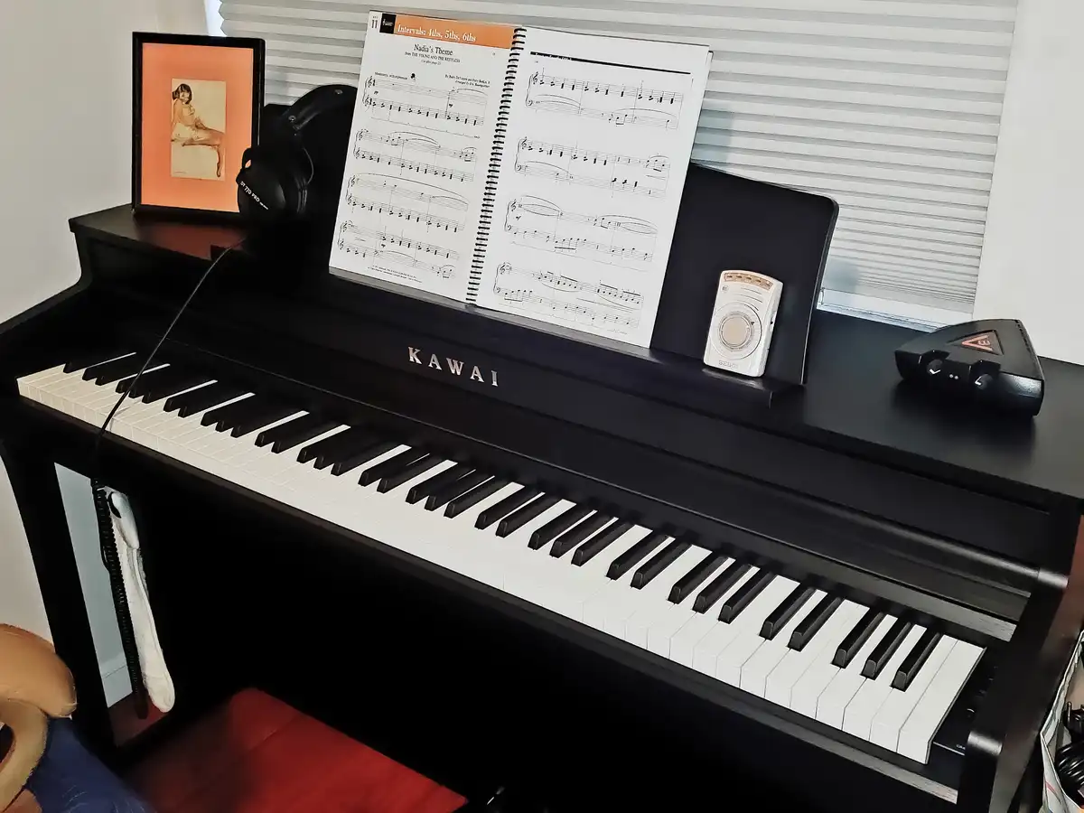 A black Kawai digital piano with sheet music for 'Nadia's Theme' from 'The Young and the Restless' on the stand, alongside a…