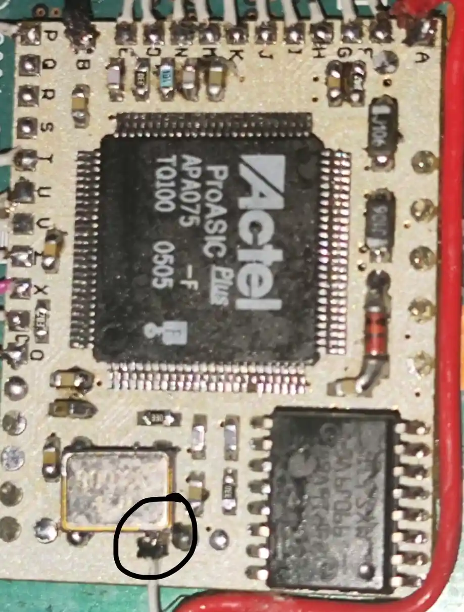 A close-up photo of an electronic circuit board featuring a black Actel ProASIC Plus APA075 chip with visible text. A small…