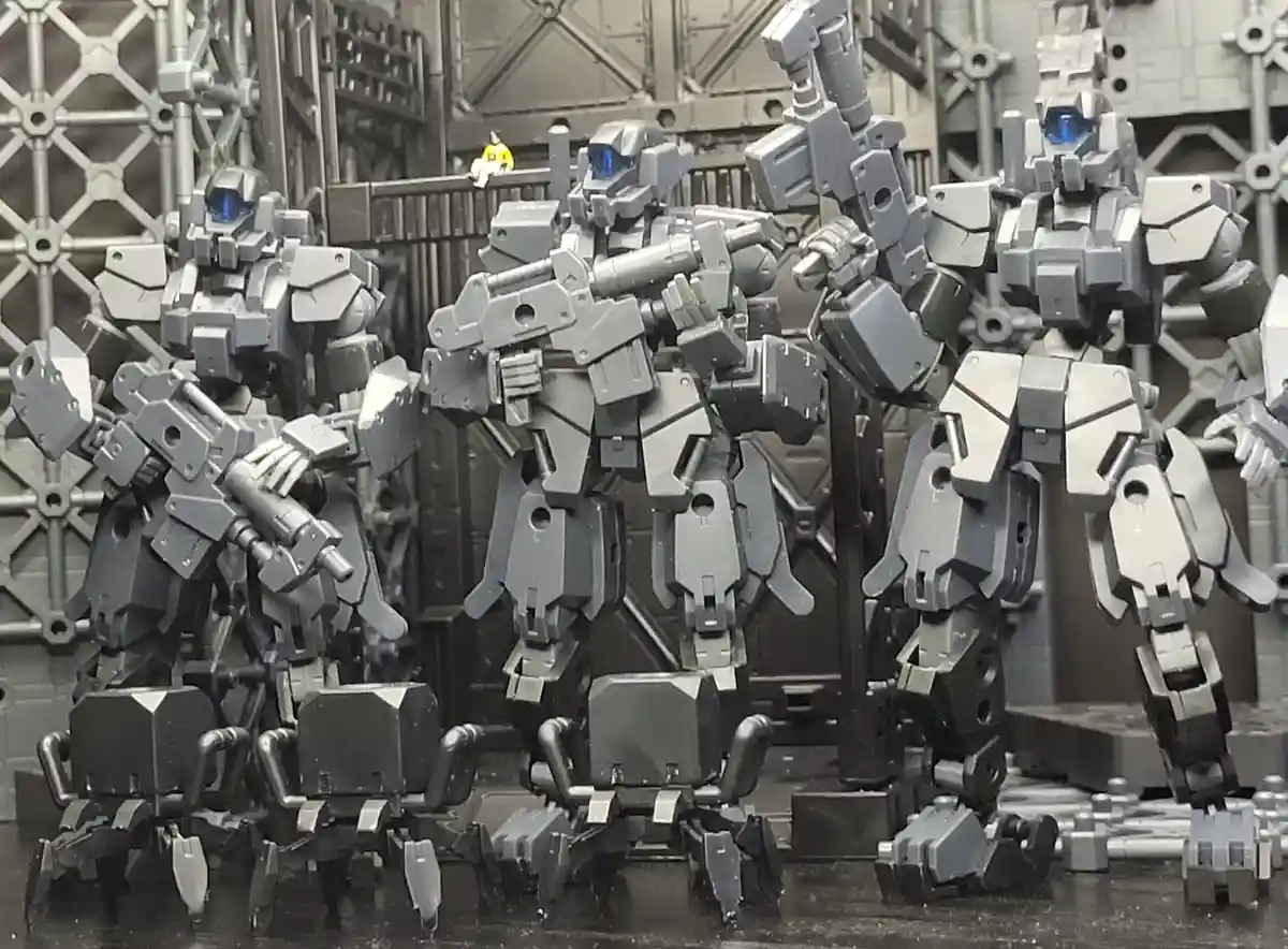 The image shows several large, grey, blocky robot models standing in a row in what appears to be a futuristic industrial…