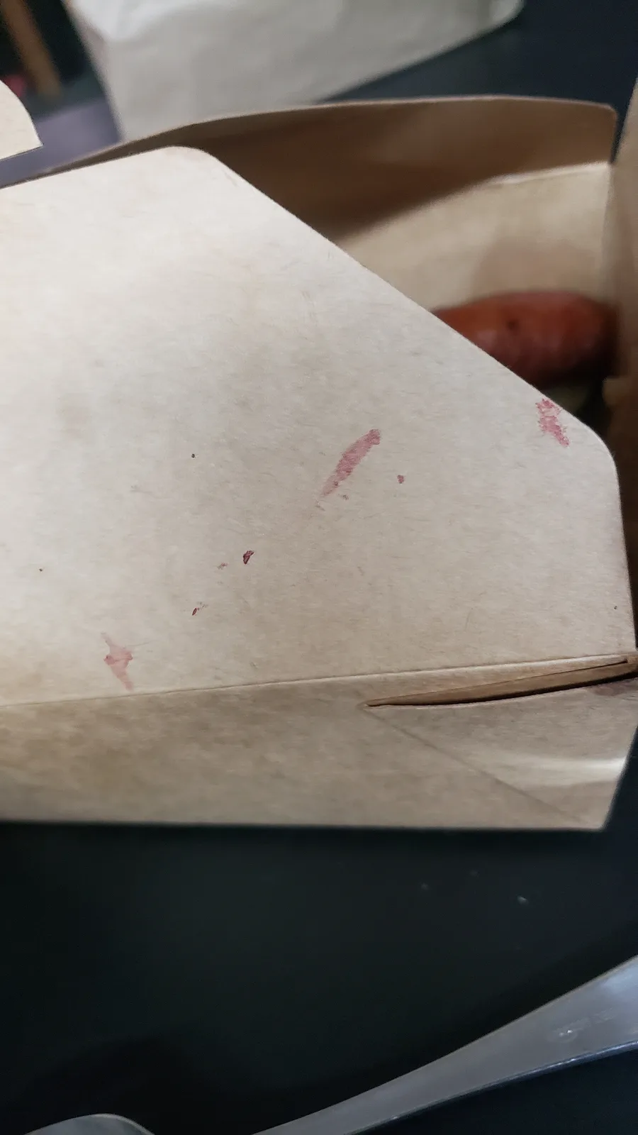 A close-up photo shows the inside of a brown paper food container with several reddish-brown smudges and stains on the lid…