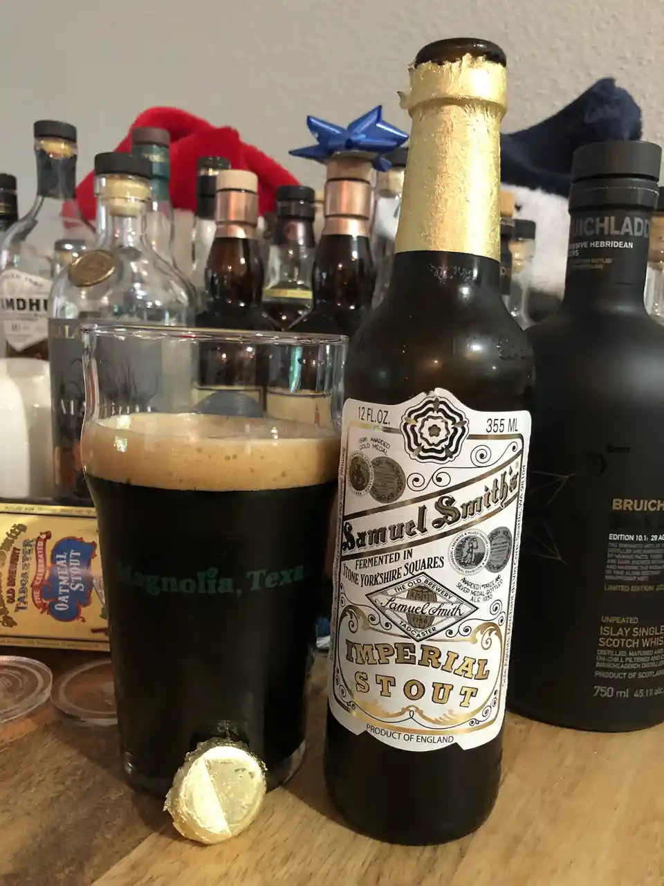 A bottle of Samuel Smith's Imperial Stout stands next to a full glass of the dark beer, with a gold-wrapped chocolate at its…