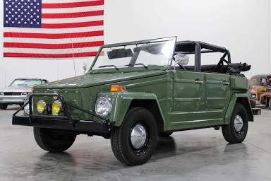 a green 1970s military-style vehicle, resembling a willys mb, is parked indoors with an american flag hanging on the wall…