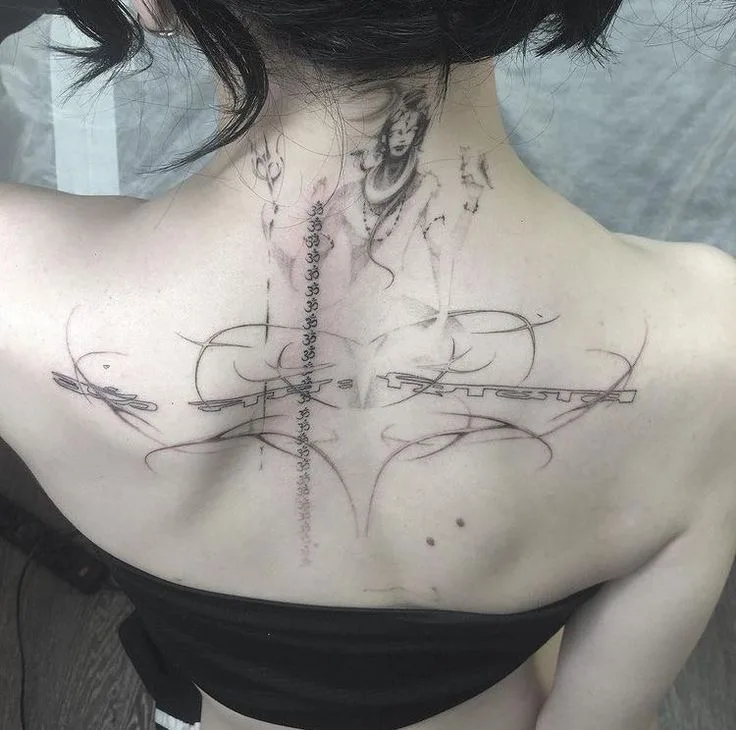 A person's upper back and neck display a large, intricate black-and-gray tattoo featuring a stylized female figure, abstract…