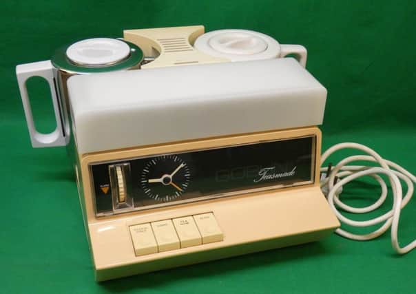 A vintage cream-colored electric tea maker with a built-in analog clock and four buttons sits on a green background. The…