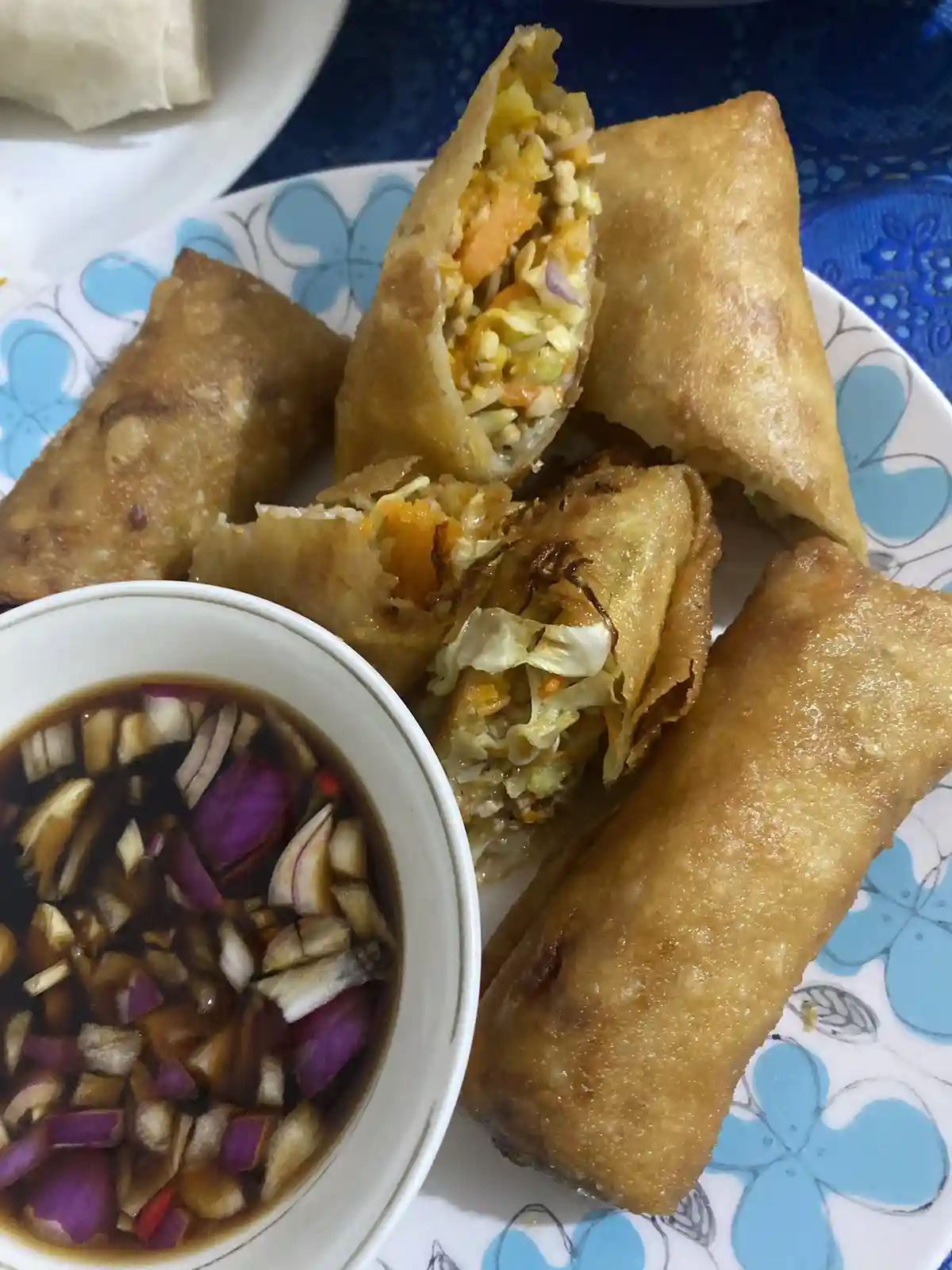 A plate of golden-brown fried spring rolls, some cut open to show a filling of shredded cabbage, carrots, and other…