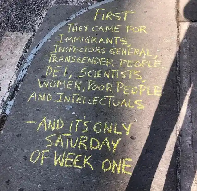 Yellow chalk text on a dark concrete sidewalk reads: 'FIRST THEY CAME FOR IMMIGRANTS, INSPECTORS GENERAL, TRANSGENDER…