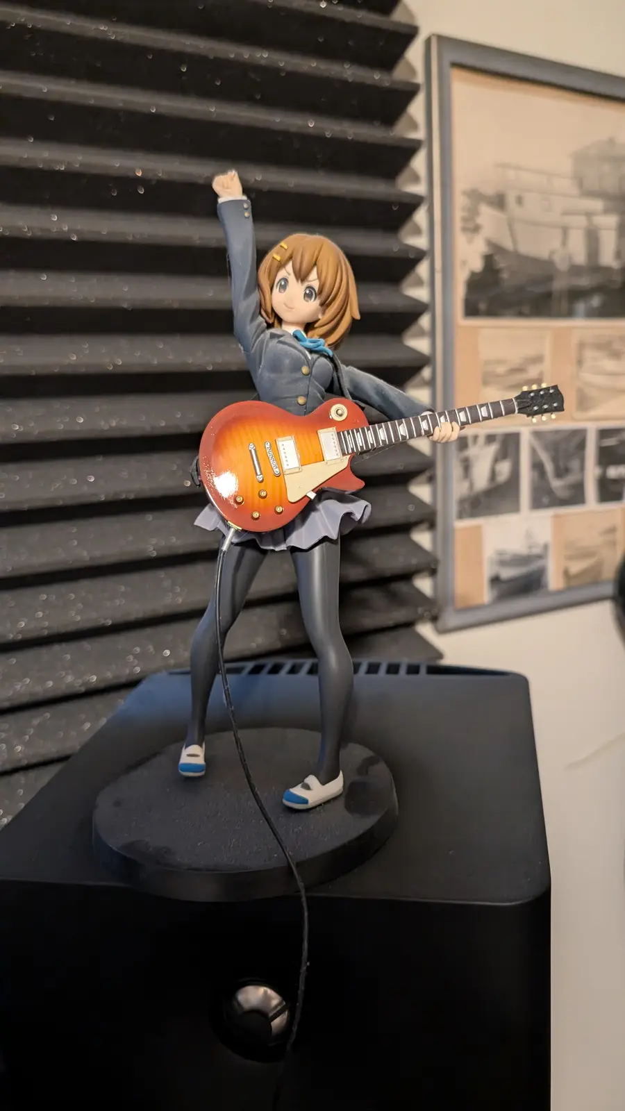 A figurine of an anime girl in a school uniform holding a red electric guitar, one arm raised in a triumphant pose, standing…