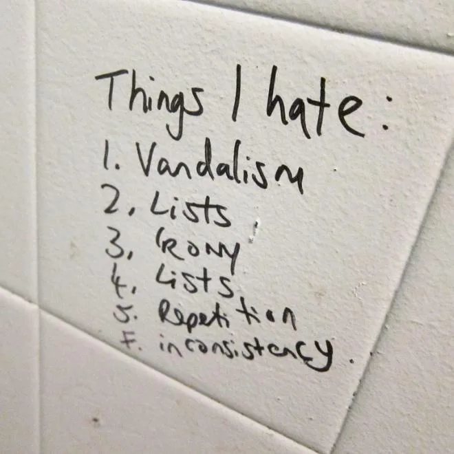 A handwritten note on a white tiled wall lists things the writer hates, including vandalism, lists, irony, lists again…
