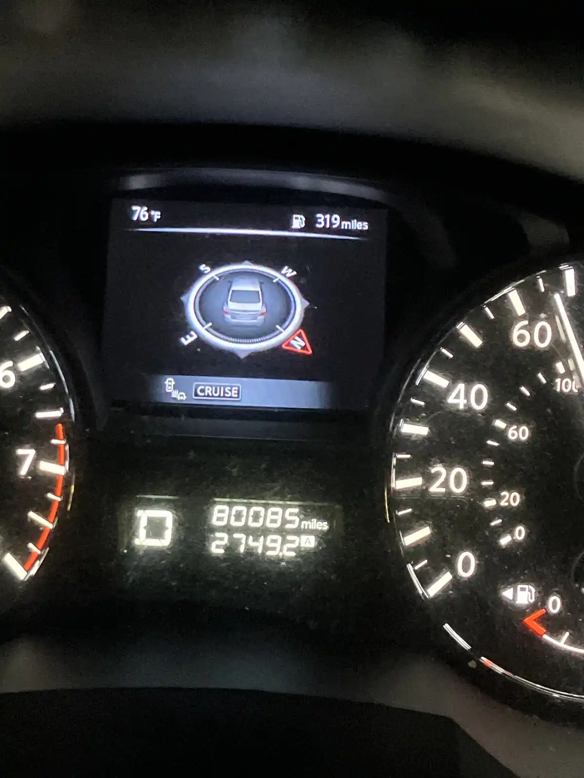 A close-up of a car's illuminated dashboard at night, showing a digital display with a compass, 'CRUISE' mode, and a warning…