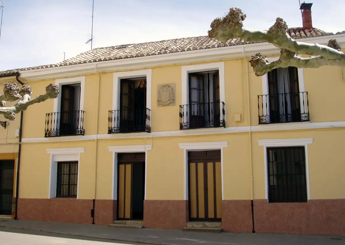 a yellow two-story building with white trim, black wrought iron balconies, and a tiled roof, with gnarled tree branches…