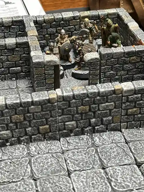 A photo of miniature fantasy figures—fighters, a wizard, and a cleric—standing inside a stone-walled dungeon room on a…