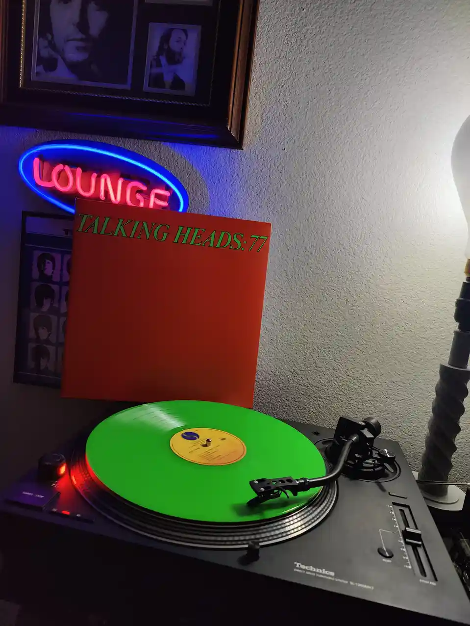 A bright green vinyl record spins on a Technics turntable, with its orange album cover standing upright behind it. The cover…