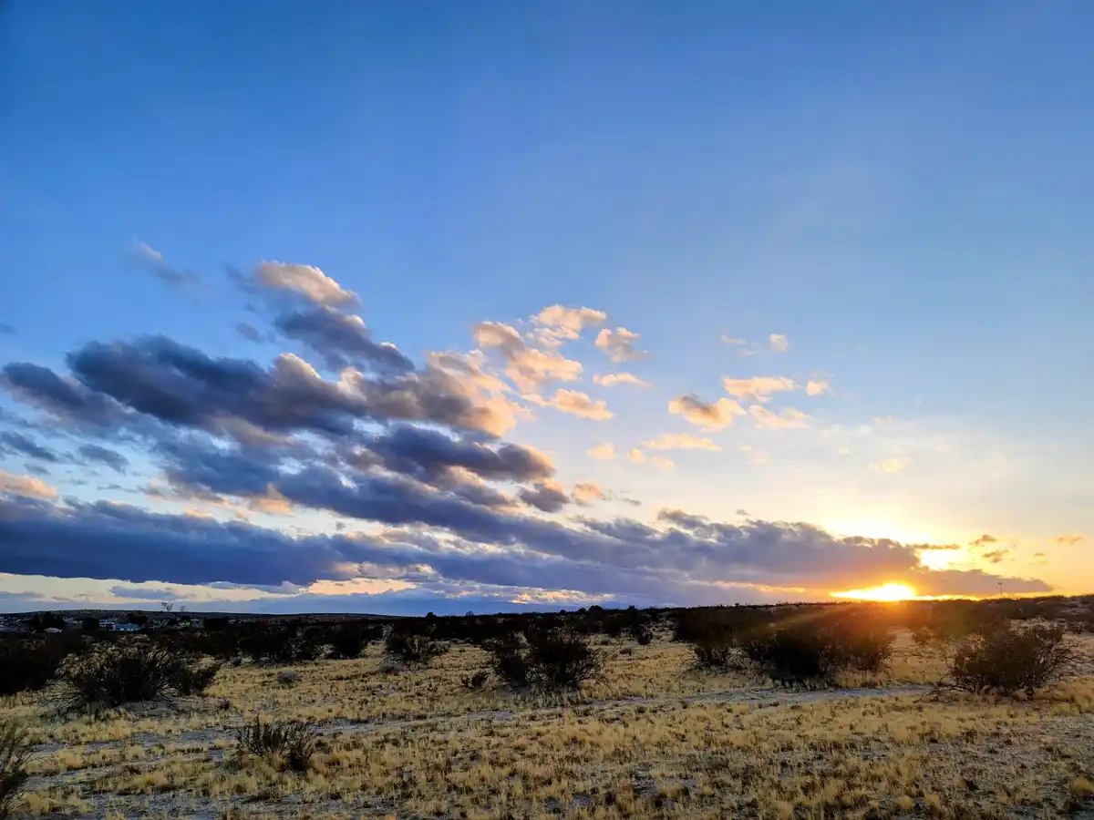A wide-angle photograph captures a serene desert sunset with the sun low on the horizon, casting golden light across…