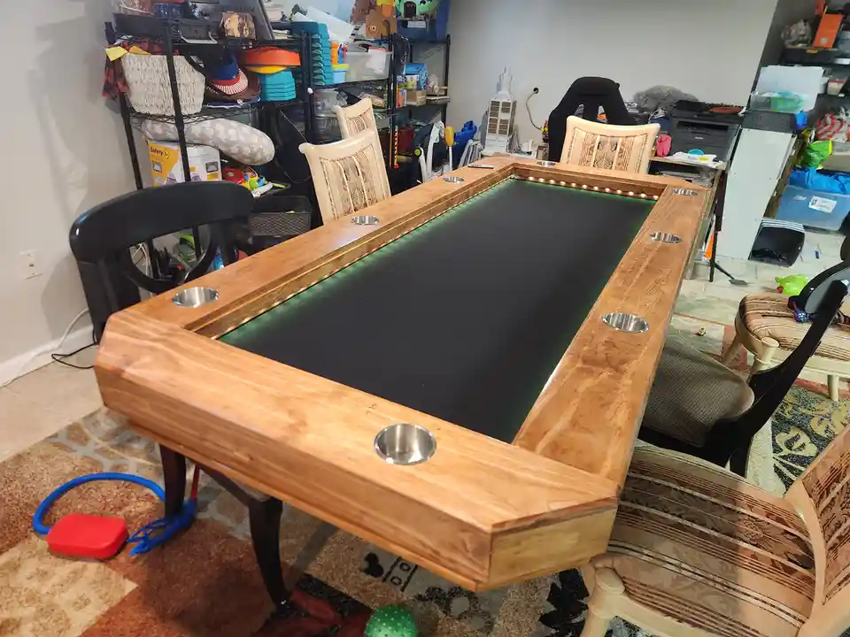 A custom-built wooden table with a green felt surface and embedded metal cup holders along its edges, surrounded by…
