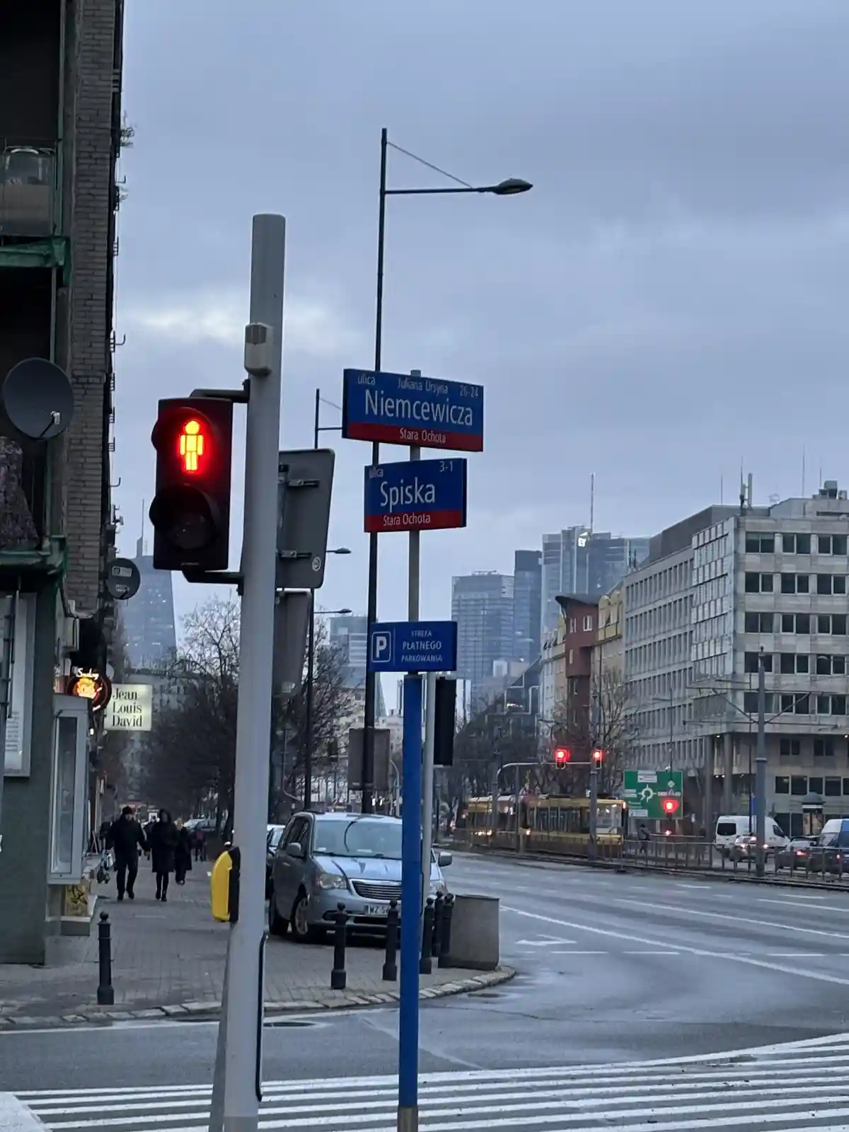 A street scene in Warsaw, Poland, featuring a red pedestrian crossing signal, street signs for 'Niemcewicza' and 'Spiska' in…
