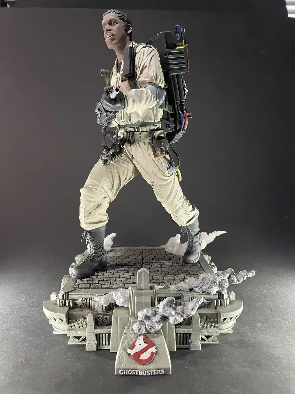A detailed Ghostbusters action figure of Ray Stantz in his iconic proton pack and jumpsuit, posed dynamically on a stone…