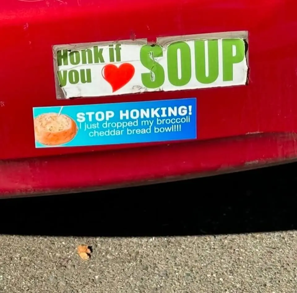 A close-up of two stickers on a red car bumper. The top sticker reads 'Honk if you ❤️ SOUP' in green and red text. Below it…