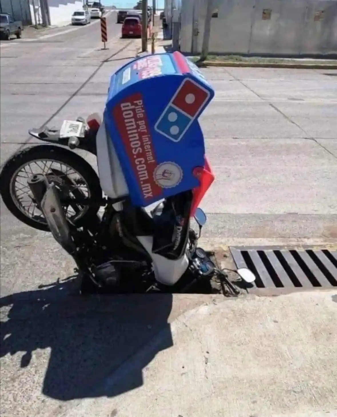 A Domino's pizza delivery motorcycle is shown crashed and upright on its front wheel, with its large blue and red branded…