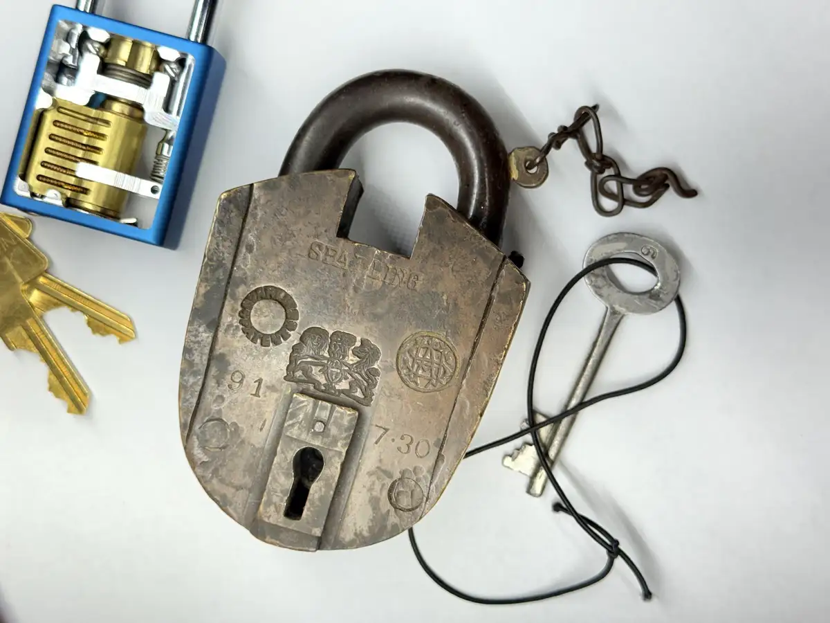 A close-up photo shows a large, old, ornate brass padlock with a keyhole and embossed designs, surrounded by various keys…