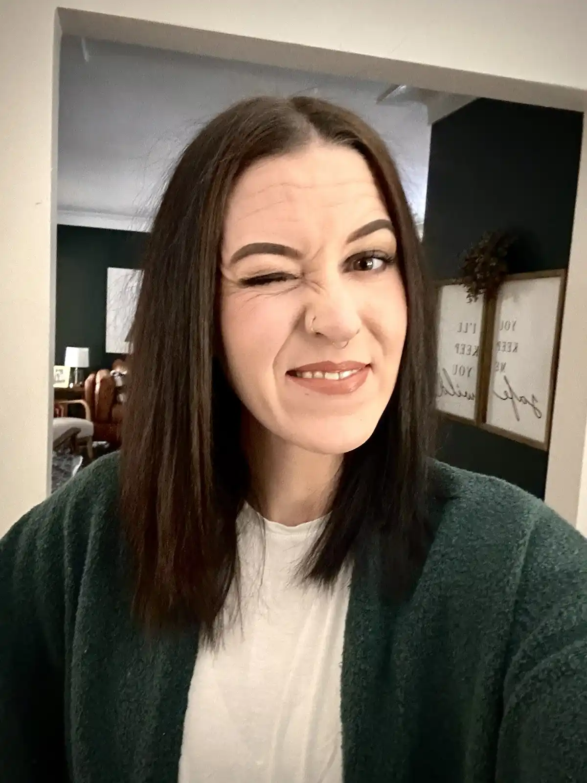 A woman with dark hair and a nose ring makes a comically exaggerated crying face, winking one eye and scrunching her nose…