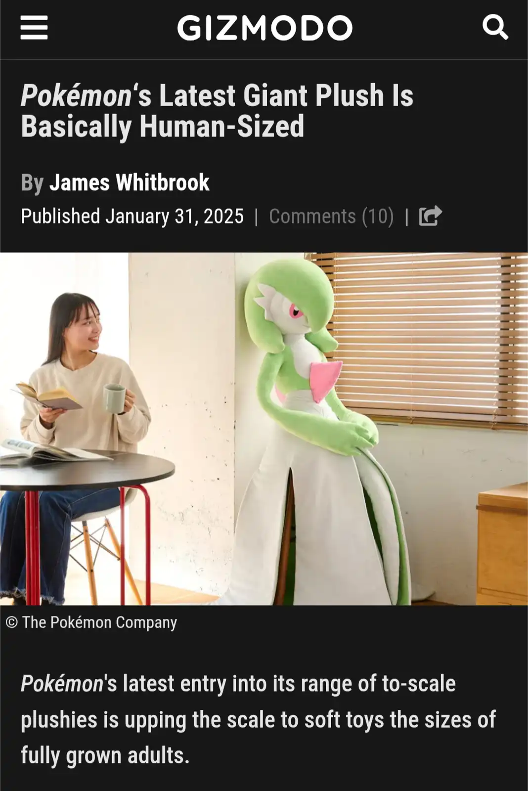 A woman sits at a table reading a book while smiling at a giant, human-sized plush toy of the Pokémon Serperior standing…