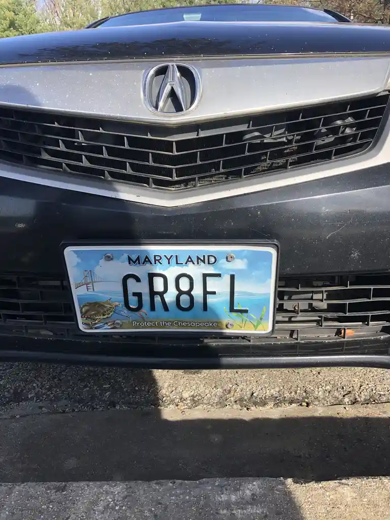 A close-up photo of the front of a black Acura vehicle showing its Maryland license plate with the registration number…