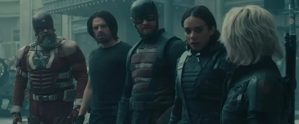A still from a movie shows five characters in tactical gear standing in a line, looking concerned. From left to right: a man…