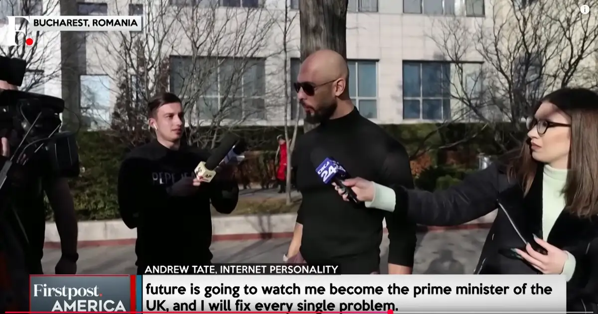 A bald man with a beard and sunglasses, identified as Andrew Tate, an internet personality, is being interviewed outdoors in…