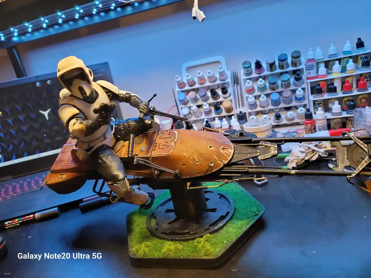 A detailed model of a Star Wars clone trooper riding a heavily weathered and battle-damaged speeder bike, mounted on a green…