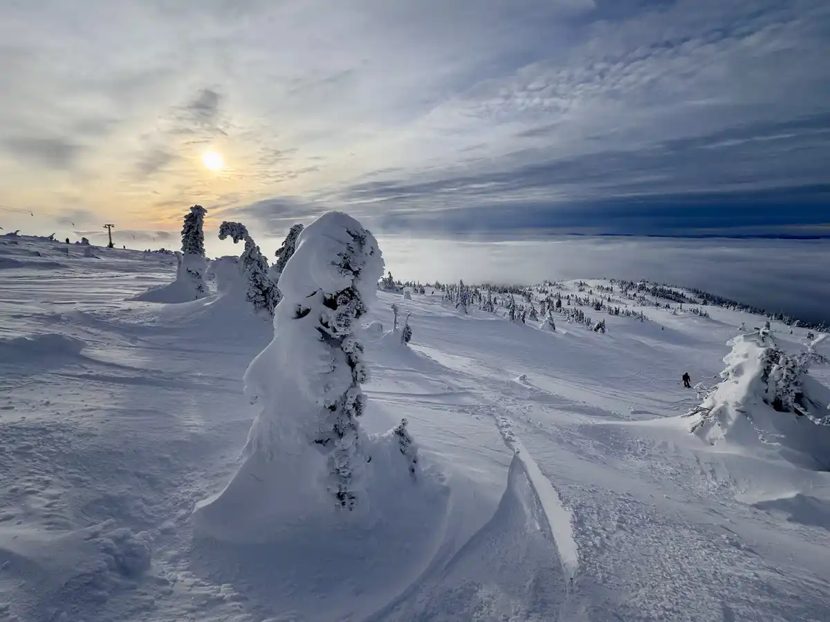 A breathtaking snowy mountain landscape at sunrise, with snow-covered trees and a skier in the distance, overlaid with the…