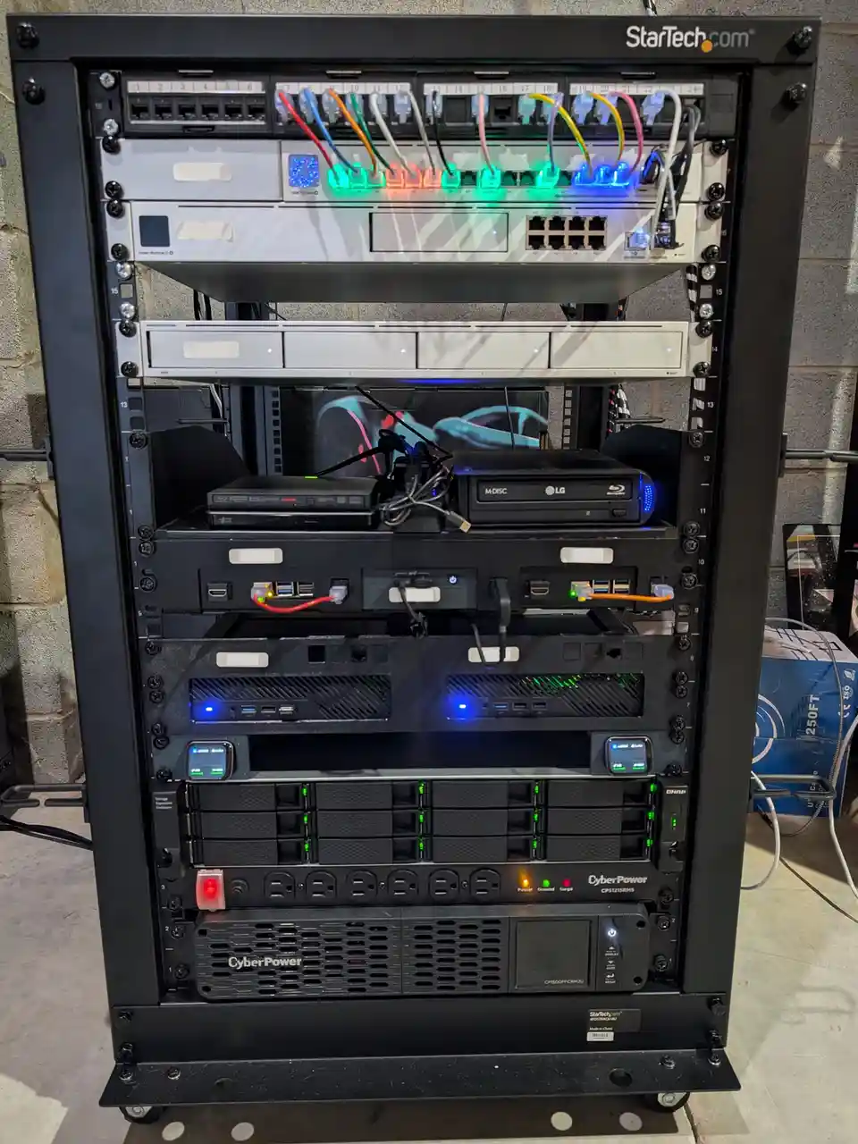 A black server rack filled with various electronic devices including a network switch with colorful lit ports, a Blu-ray…