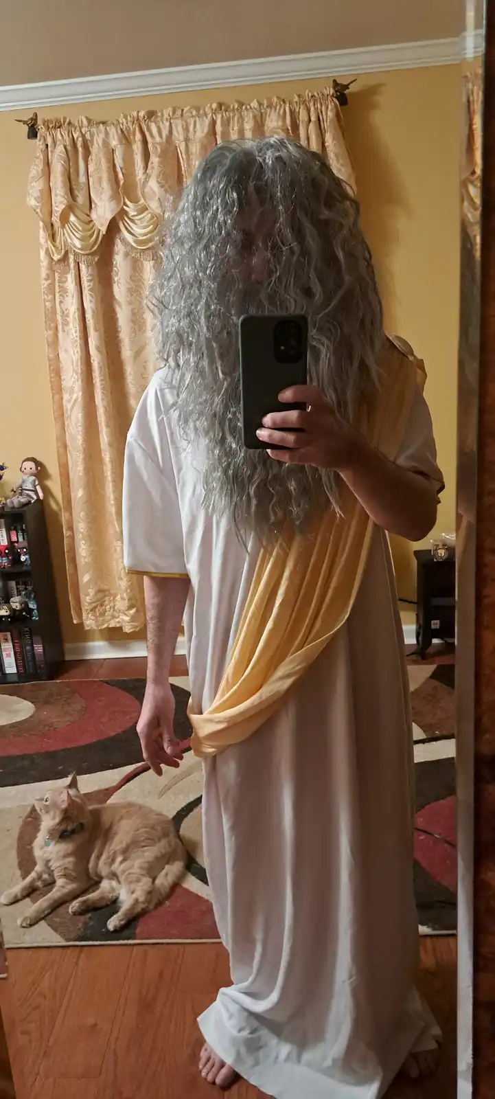 A person in a homemade ancient Greek or Roman costume, featuring a long white tunic with a yellow sash and a voluminous grey…