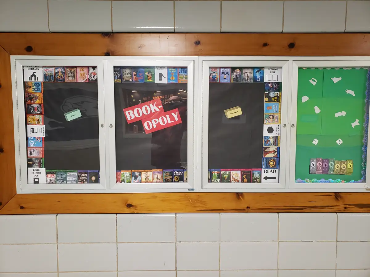 A library display case is creatively transformed into a Monopoly board game, with book covers replacing property cards, a…