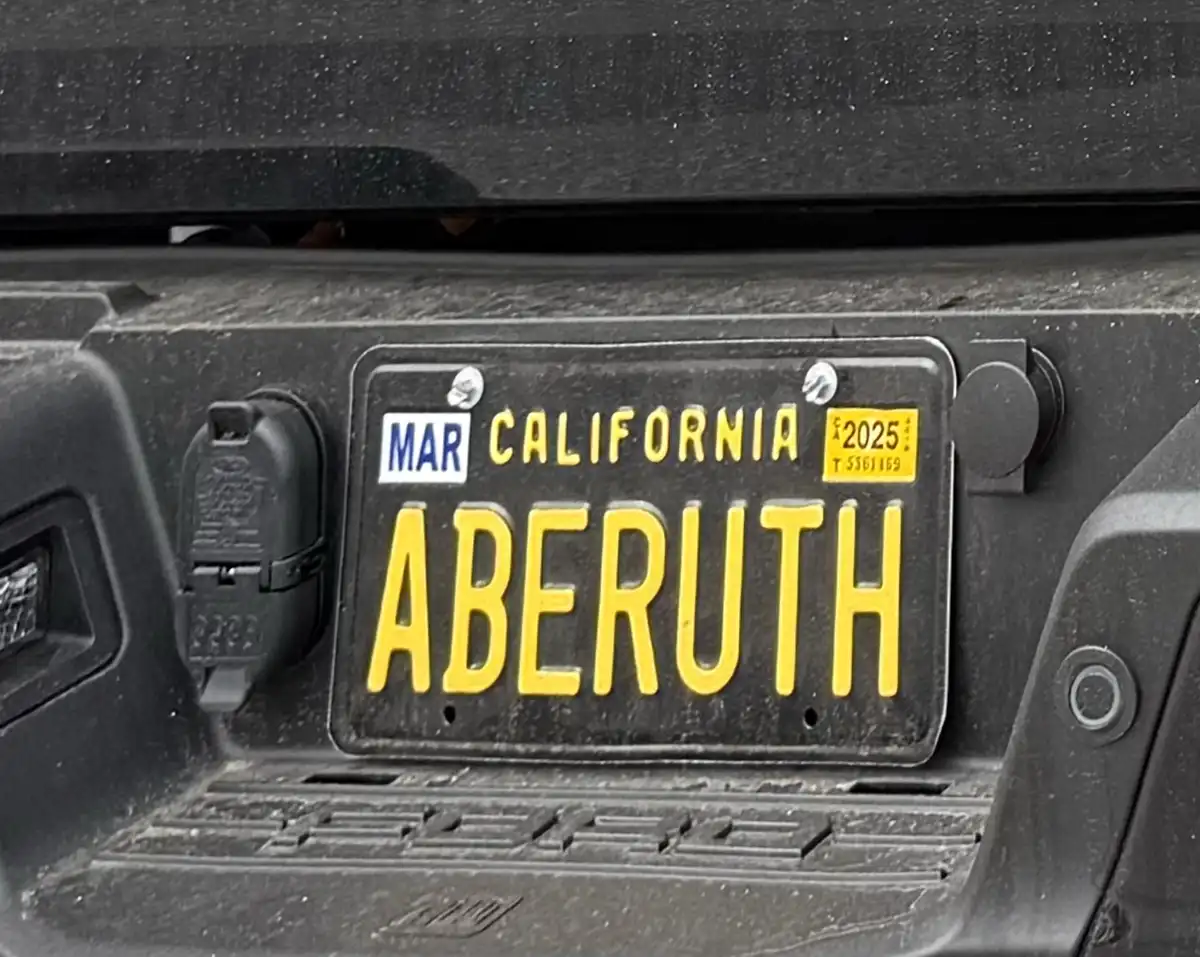 A close-up photo of a California license plate mounted on the rear of a dark-colored vehicle, showing the registration…