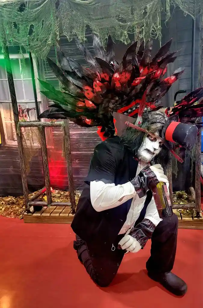 A person in a Halloween costume with a large, elaborate black and red feathered headdress, white face paint, and a top hat…