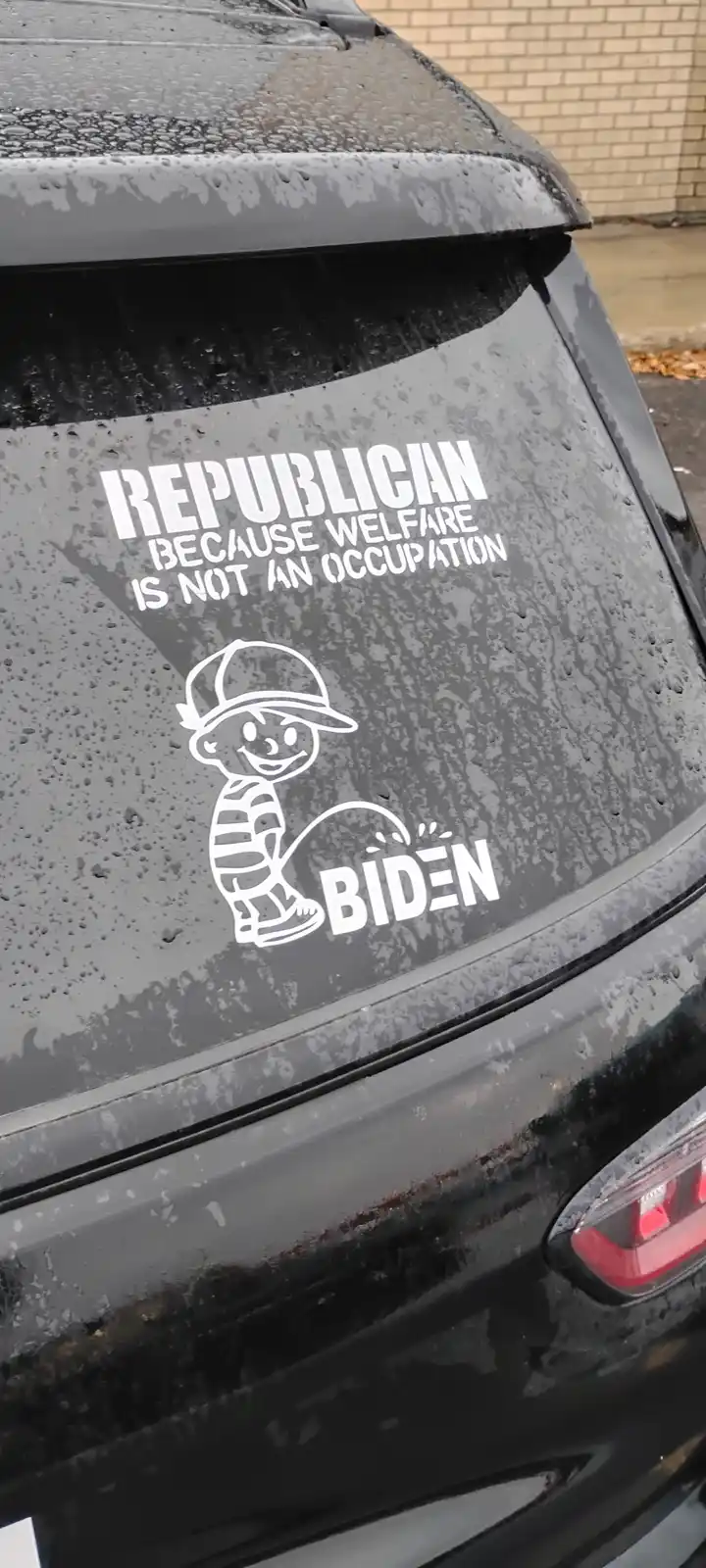 A white sticker on the rear window of a black car covered in rain droplets features the text 'REPUBLICAN BECAUSE WELFARE IS…