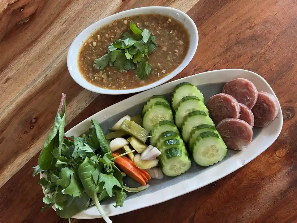 An overhead photo shows a meal on a wooden table: a bowl of brown dipping sauce with cilantro, and a long plate with sliced…