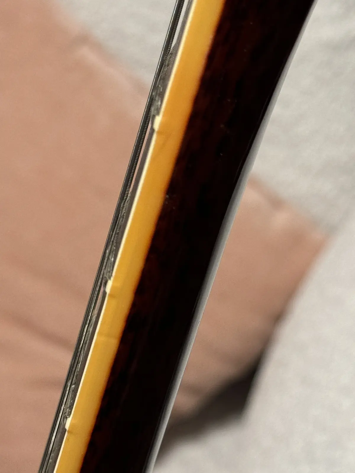 A close-up photo shows the edge of a dark brown guitar body with a light amber binding, revealing a small, noticeable chip…