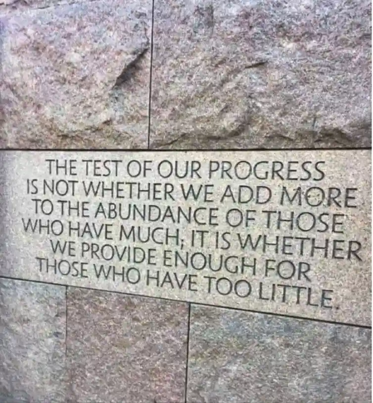 A close-up photo of engraved text on a granite stone wall, which reads: 'THE TEST OF OUR PROGRESS IS NOT WHETHER WE ADD MORE…