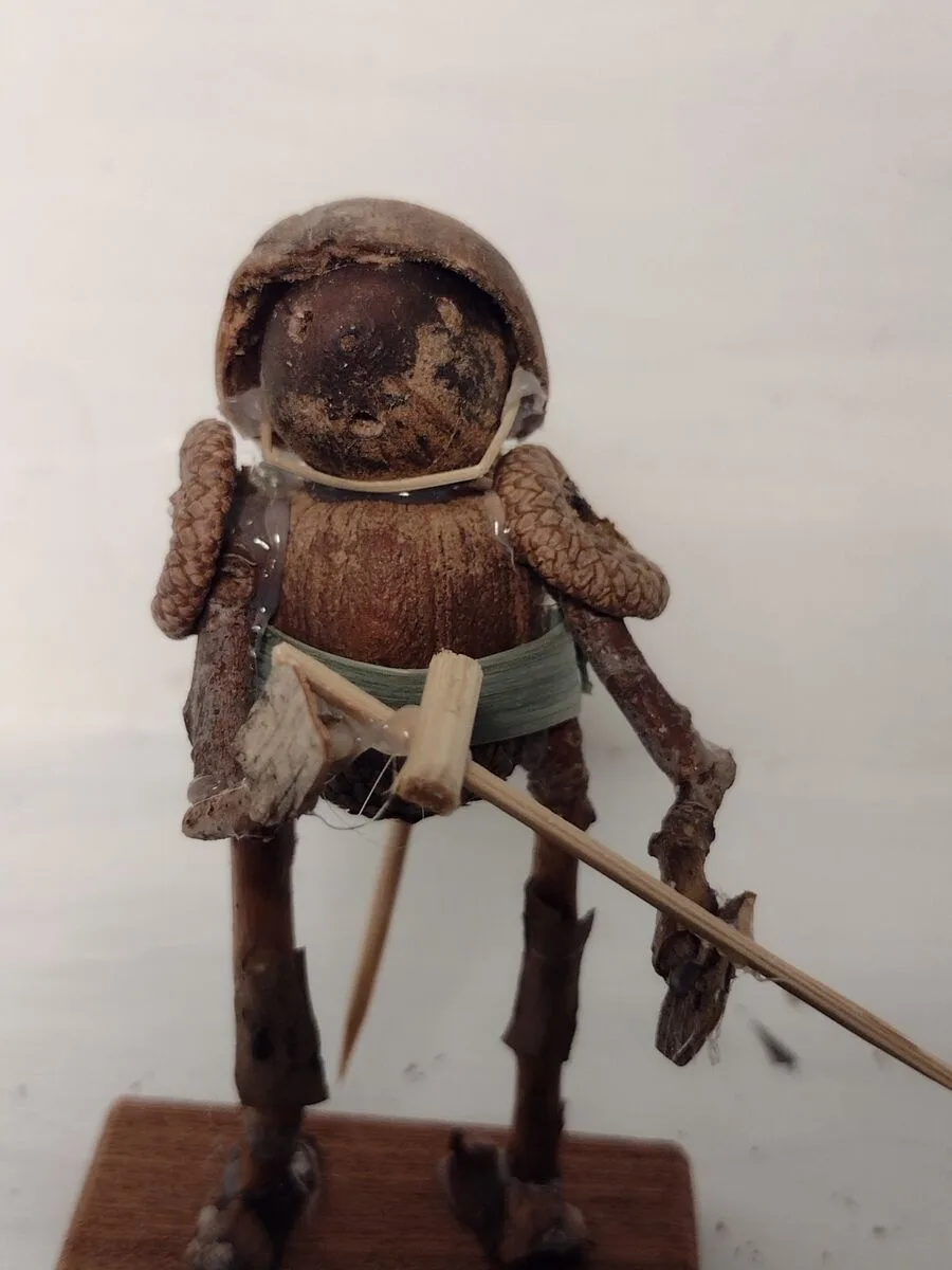 A handmade figurine crafted from natural materials like pinecones, twigs, and bark, resembling a soldier wearing a helmet…