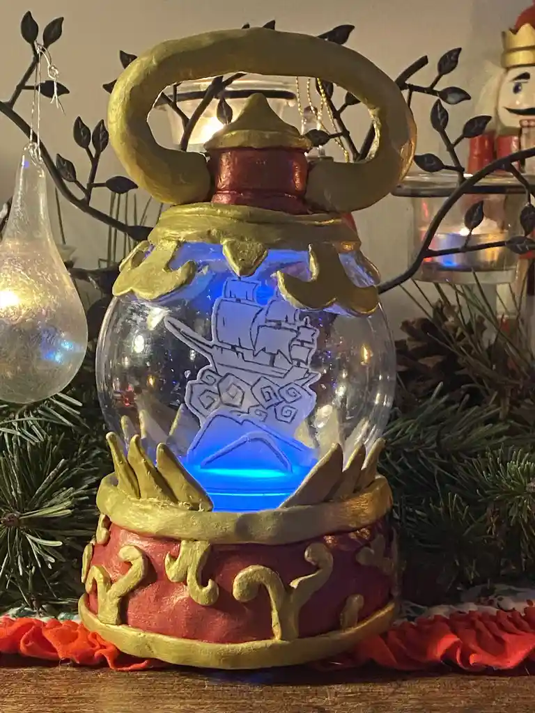 A decorative, ornate lantern with a glass globe containing a blue-lit, etched image of a ship sinking into waves. The…