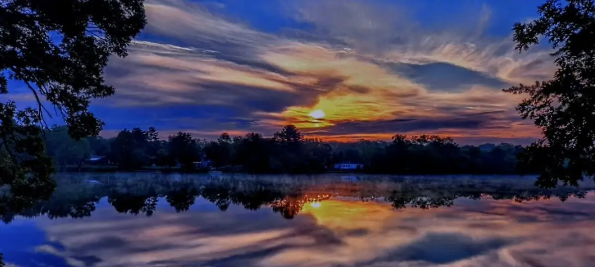 A serene sunset over a calm lake with trees framing the shot, the sky reflecting in the water. Overlaid text reads: 'i'm not…