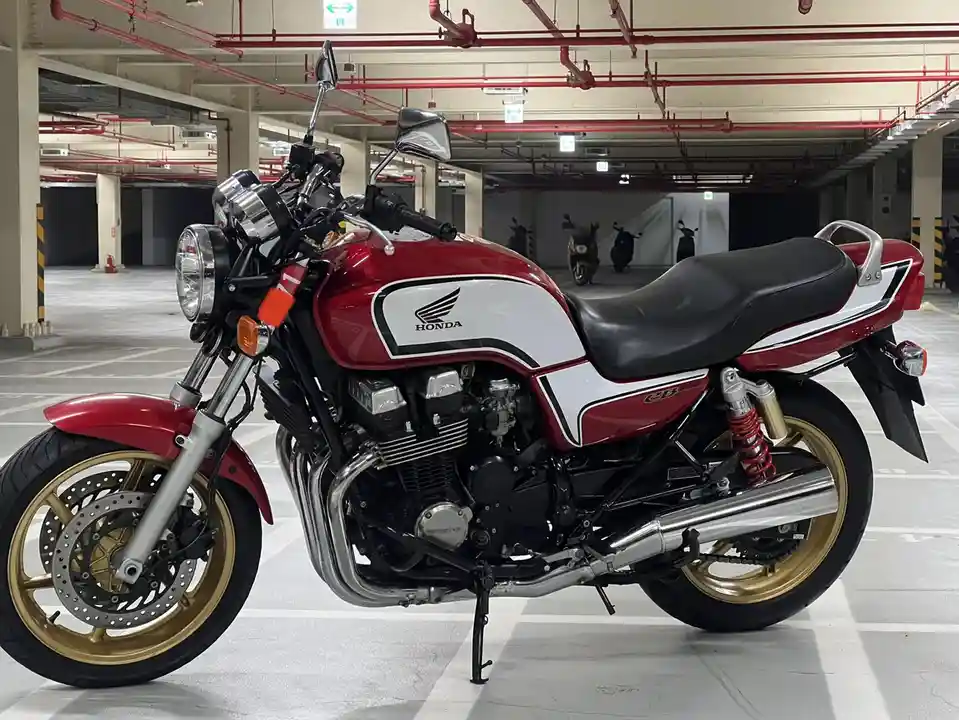 a red and white honda cb750 motorcycle with gold rims is parked in an underground parking garage, with red pipes and pillars…