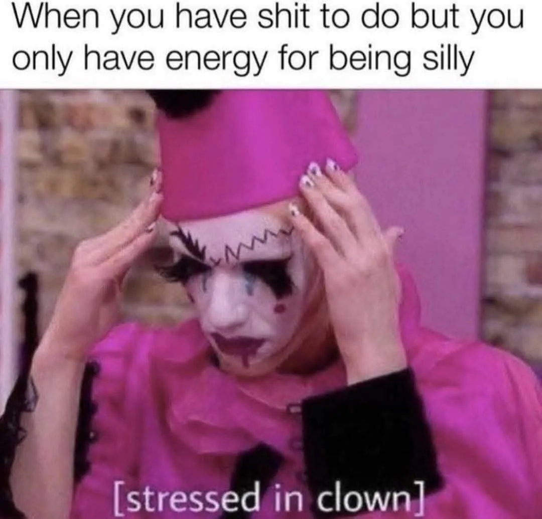 A person dressed as a clown in a pink outfit and hat, with white face paint, black markings around the eyes, and red lips…