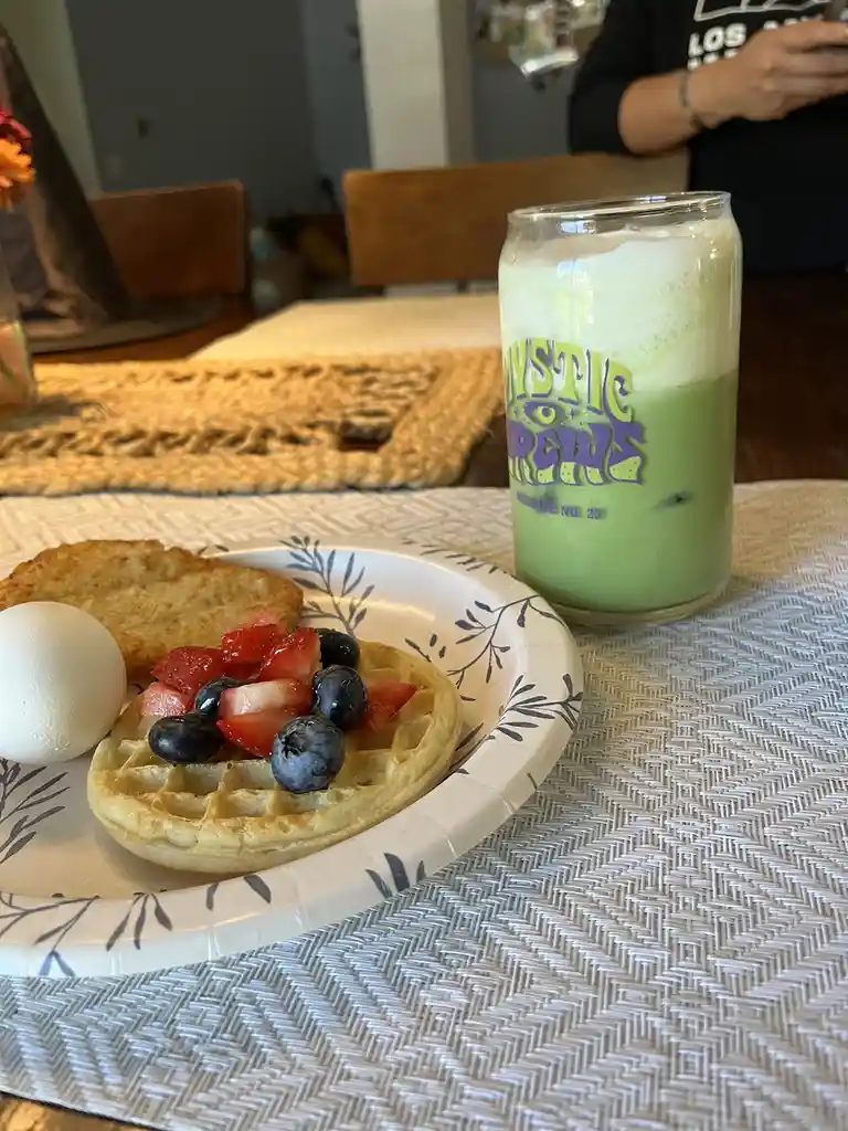 A breakfast scene shows a plate with a waffle topped with strawberries and blueberries, a boiled egg, and a hash brown…